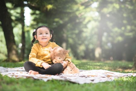 Little asian girl hugging her teddy bear in a park. Concept of happiness and childhoodの写真素材