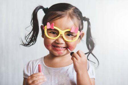 Cute little asian girl playing with toy make up and applying lipstick to her lips. Concept of beauty and childhoodの写真素材