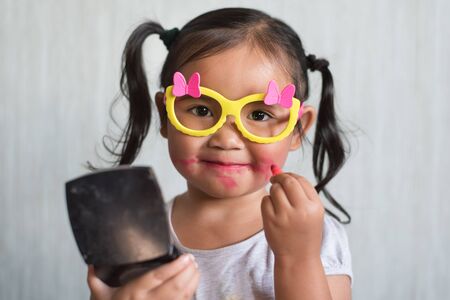little asian girl playing with makeup blusher brush with dingy face. Concept of beauty and childhoodの写真素材