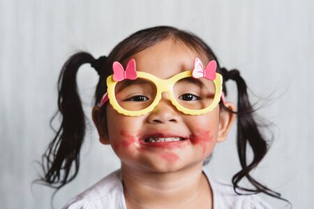 Cute little asian girl playing with lipstick makeup and applying lipstick to her lips. Concept of beauty and childhoodの写真素材