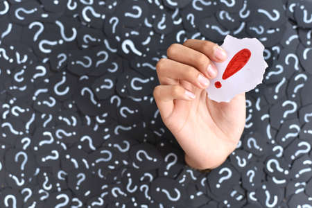Hand holding an Exclamation Mark against Question Mark backgrounds. Concept of FAQ, Q&A and Answersの写真素材