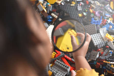 little girl child hand holding magnifying glass looking on a plastic toy block. Concept of creativity and childhoodのeditorial素材
