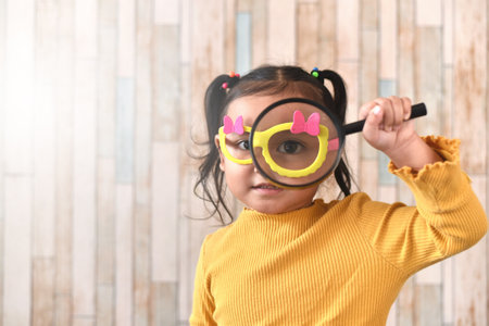 Cute little asian girl looking through a magnifying glass. Concept of curiosity child learning and eyesightの写真素材