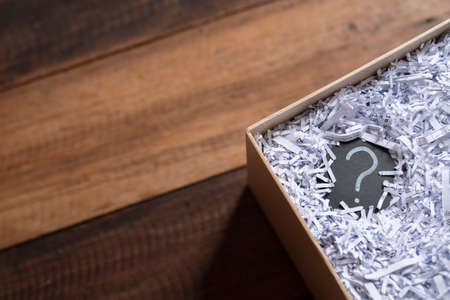 Question mark in a box with shredded paper on wooden table. Concept of suprise, delivery, shipment and questionsの写真素材