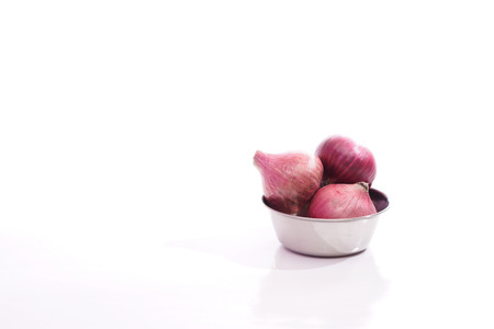 Red onion in a steel bowl over white background.の写真素材