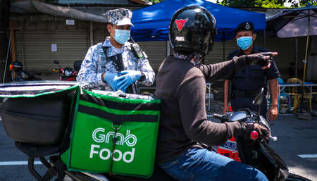 KUALA LUMPUR, MALAYSIA - APRIL 18, 2020 : Malaysia soldier officer inspect road users at a roadblock to enforce the order to stay at home, during the 'movement control order' COVID-19 outbreak.のeditorial素材