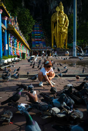 BATU CAVES, MALAYSIA - JANUARY 08, 2020 : A boy play bird at the famous and iconic limestones with new rainbow painting at Batu Caves. The cave is the focal point of Hindu festival of Thaipusam and Deepavali in Malaysia.のeditorial素材