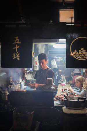 Worker of the restaurant preparing the food for the customer at traditional bar in Omoide Yokocho, Shinjuku. Portrait Orientation.のeditorial素材