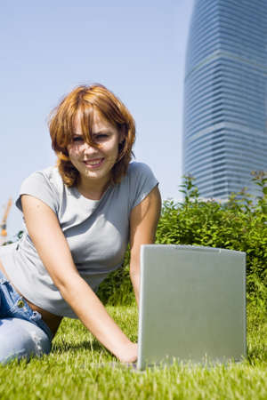 young girl with laptop on the grass before office buildingの写真素材
