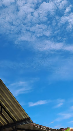 A bright blue sky with white clouds and a roof in the corner