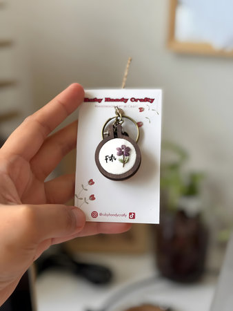 Person holding a keychain with a floral pattern on a white card