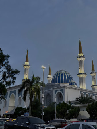 A serene mosque with multiple minarets and a large dome, surrounded by trees and cars in the...