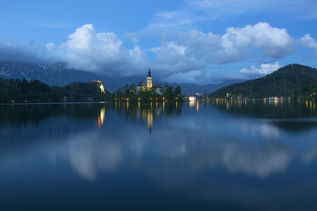 Island on Bled lake and pilgrimage church of the Assumption of Mary reflected in water with moving...