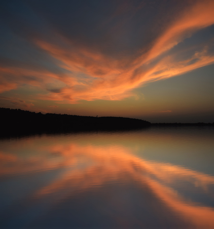 Beautiful majestic sunset clouds over lake with reflection in waterの写真素材