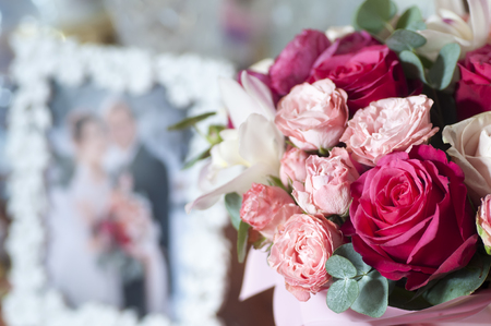 Bridal bouquet of red, pink and white roses near photo of newlyweds in frameの写真素材