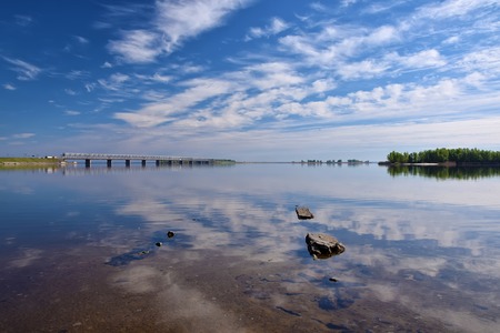 Beautiful clouds reflected in surface water at sunny summer day. Bridge and dam across the Dnieper river, Cherkasy, Ukraineの写真素材