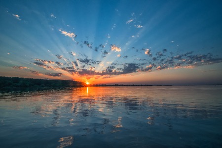 Amazing sunset over the river. Beautiful clouds, picturesque sunbeams and colorful reflection in the...