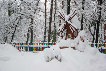 Decorative windmill and gnome covered with fresh snow in winter park.の写真素材