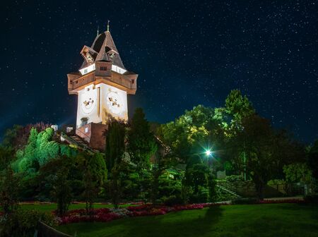 Scenic night view of famous Grazer Uhrturm (clock tower) in flower garden on Schlossberg hill under starry sky, Graz, Austria. Uhrturm is a main symbol of Graz.の写真素材