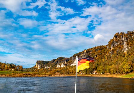 Picturesque atumn scenery with waving National Flag of Germany. View over river Elbe. National Park Saxon Switzerland, Germanyの写真素材