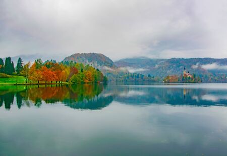 Autumn scenery of colorful trees and Bled island with Pilgrimage Church reflected in surface water of the lake. Bled Lake, Sloveniaの写真素材