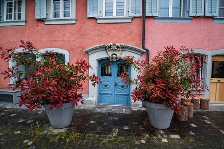 Beautiful baroque door in old house and two flowerpots with red leaf plants on wet pavement, Zug, Switzerlandの写真素材