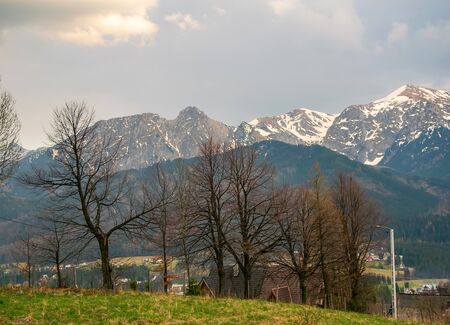 Scenic view of Koscielisko village near Zakopane with panorama of snow caped High Tatras and Giewont mountain on background. Bare trees on foregroundの写真素材