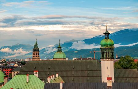 Aerial view of towers and rooftops of Court Church (Hofkirche) and Jesuit Church in old city of Innsbruck, Alps mountains in background, Tirol, Austriaの写真素材