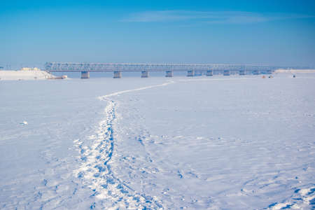 Picturesque winter scenery with road bridge across the Dnieper river near Cherkasy, Ukraine. Footpath of fishermen on river ice. Sunny winter dayの写真素材