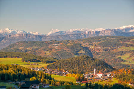 Incredible scenic view of traditional tyrol village with church in alpine valley at autumn sunny day. Snowcaped mountain range on background. Dolomites, South Tyrol, Italyの写真素材