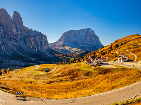 Amazing panoramic view on Sassolungo - Langkofel mountain and Gardena Pass at sunny autumn day. Winding road among yellowed pasture. Dolomite Alps, South Tyrol, Italyの写真素材