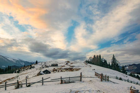 Farm on mountain range at winter evening. Picturesque clouds burning by sunset. Dzembronya, Ukrainian Carpathians.の写真素材