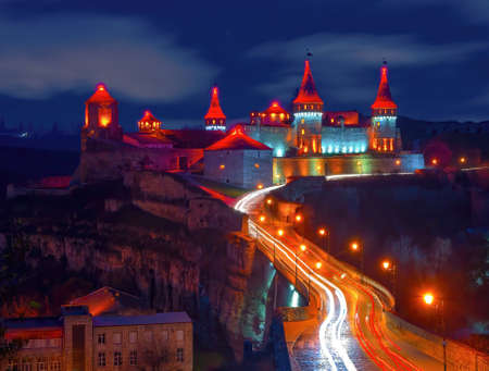 Scenic nightscape of illuminated medieval fortress of Kamianets-Podilskyi, Ukraine. Picturesque moving clouds in the night skyの写真素材