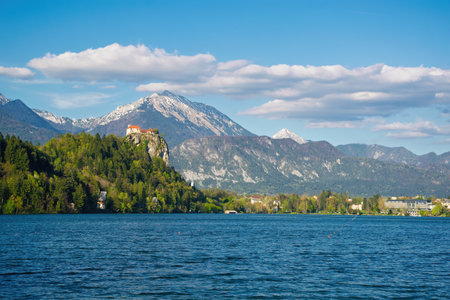 Scenic view of Bled Castle perched on a cliff overlooking the tranquil Lake Bled, with the majestic Julian Alps providing a stunning backdrop in Sloveniaの写真素材