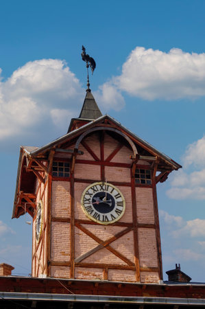 Clock tower of the Old Town Hall in Chortkiv, Ternopil region, Ukraine, showing its weather vane, clock face, and intricate architectural details under a blue sky with white cloudsの写真素材