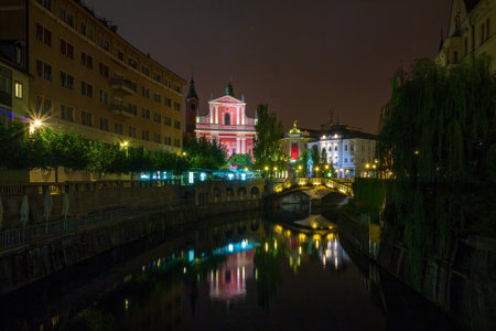 Franciscan Church of the Annunciation with Preseren Square and Triple Bridge reflecting on Ljubljanica river at night with illuminated buildings and street lights in Ljubljana, Slovenia, Europeの写真素材