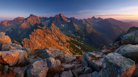An expansive view captures rugged mountain peaks under a vibrant, color-rich sky. The composition highlights the textures of the rocky foreground, contrasted against the softer gradients of the sky. The scene evokes a sense of vastness, suitable for diverse applications including travel, nature, and environmental themes.の素材