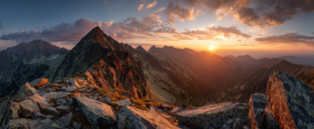 An awe-inspiring mountain landscape is bathed in warm sunlight at dusk, showcasing rugged peaks and a rocky foreground. The sky is filled with beautiful clouds, featuring hues of orange and purple. The image could be used for travel brochures, environmental campaigns, or landscape photography.の素材