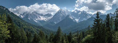 A scenic mountain range dominates the landscape, showcasing lush green trees in the foreground and majestic peaks in the distance. The sky is partly covered with white clouds, creating a contrast with the blue background. The image captures a natural setting potentially suitable for travel or environmental themes.の素材