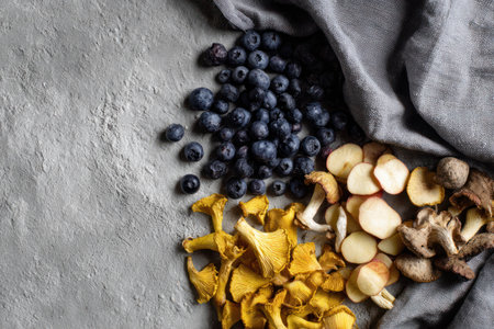 An overhead shot presents blueberries, sliced mushrooms, and golden chanterelles. A gray fabric rests beside the foods, contrasting with the textures and colors. The setting appears to be indoors, with soft lighting. This image could be utilized for culinary, dietary, or health-related publications.の素材