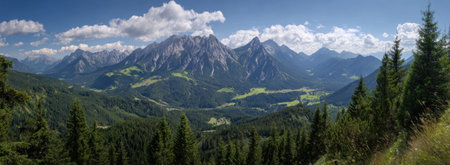 A scenic landscape presents mountains with rocky peaks, lush green forests, and a partly cloudy sky. The composition is a panoramic view, possibly taken during the day. The overall style suggests natural beauty suitable for various uses, including travel promotions and environmental themes.の素材