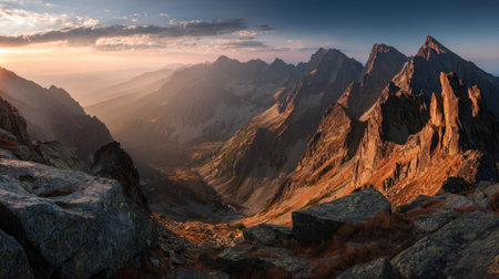 The image captures a vast mountain range under a dramatic sunset sky. The scene is filled with the textured details of the rocks and mountains. Warm sunlight bathes the peaks, creating a contrast with the shadows. This landscape could be used for environmental or travel content.の素材
