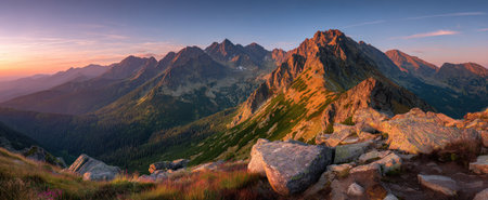 The image features a vast mountain range under a colorful sunrise. Golden sunlight bathes the peaks, highlighting rocky textures and lush greenery. The panoramic view creates a sense of grandeur and tranquility. Ideal for use in environmental articles, travel brochures, and other commercial purposes.の素材