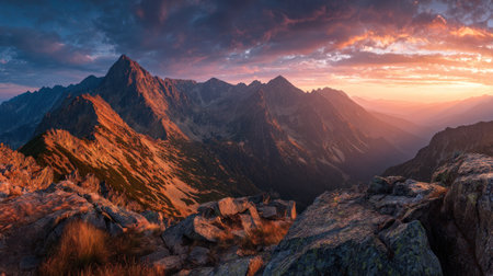 The image presents a stunning mountain landscape bathed in the warm glow of sunset. The composition features rugged peaks under a dramatic sky displaying a gradient of colors. The foreground consists of textured rocks. This visual would be suitable for various commercial and editorial purposes such as websites or prints.の素材