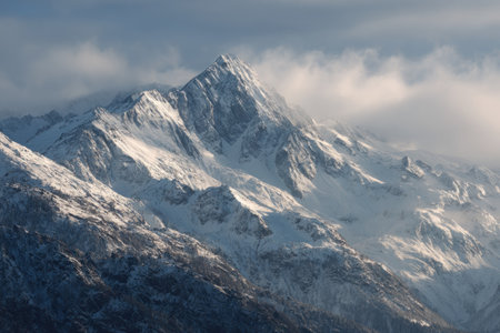 The image presents a snow-covered mountain, its peak piercing through a cloudy sky. The composition showcases textured surfaces and variations of white, gray, and brown. It evokes a sense of natural beauty, potentially suitable for environmental or adventure-themed content.の素材