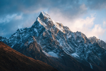 A majestic mountain peak covered in snow stands tall under a cloudy sky. The image showcases the rugged texture of the mountain, with colors ranging from dark browns to bright white. Ideal for a variety of commercial applications, the composition suggests a natural environment under daylight.の素材