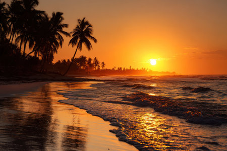 A vibrant sunset illuminates a tropical beach scene. Palm trees silhouette against the orange sky, while waves gently roll onto the shore. The warm colors and soft lighting create a peaceful atmosphere. This image is suitable for travel, tourism, or environmental themes.の素材