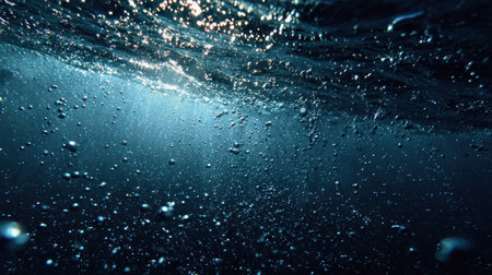 An underwater perspective reveals a dark blue environment filled with numerous bubbles. The composition captures the interplay of light filtering down, illuminating the scene. This tranquil visual can be used for various editorial or commercial projects. The textures create a sense of depth and immersion, inviting viewers to explore the depths.の素材