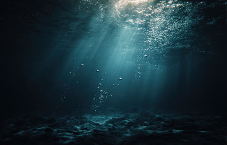 This image showcases an underwater view with sunbeams penetrating the dark, deep blue water. Bubbles rise towards the surface creating an atmospheric effect. The composition features textures and light, potentially suitable for various commercial and editorial uses. The scene suggests a natural aquatic environment.の素材