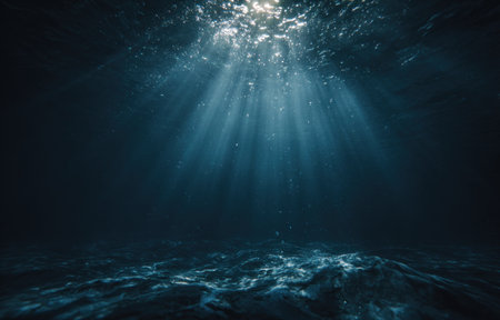 This image depicts an underwater scene with sunbeams penetrating the surface. Dark blue water creates a sense of depth and mystery. The composition emphasizes the interplay of light and shadow, suggesting a marine environment. This image is suitable for various editorial and commercial applications related to nature and exploration.の素材
